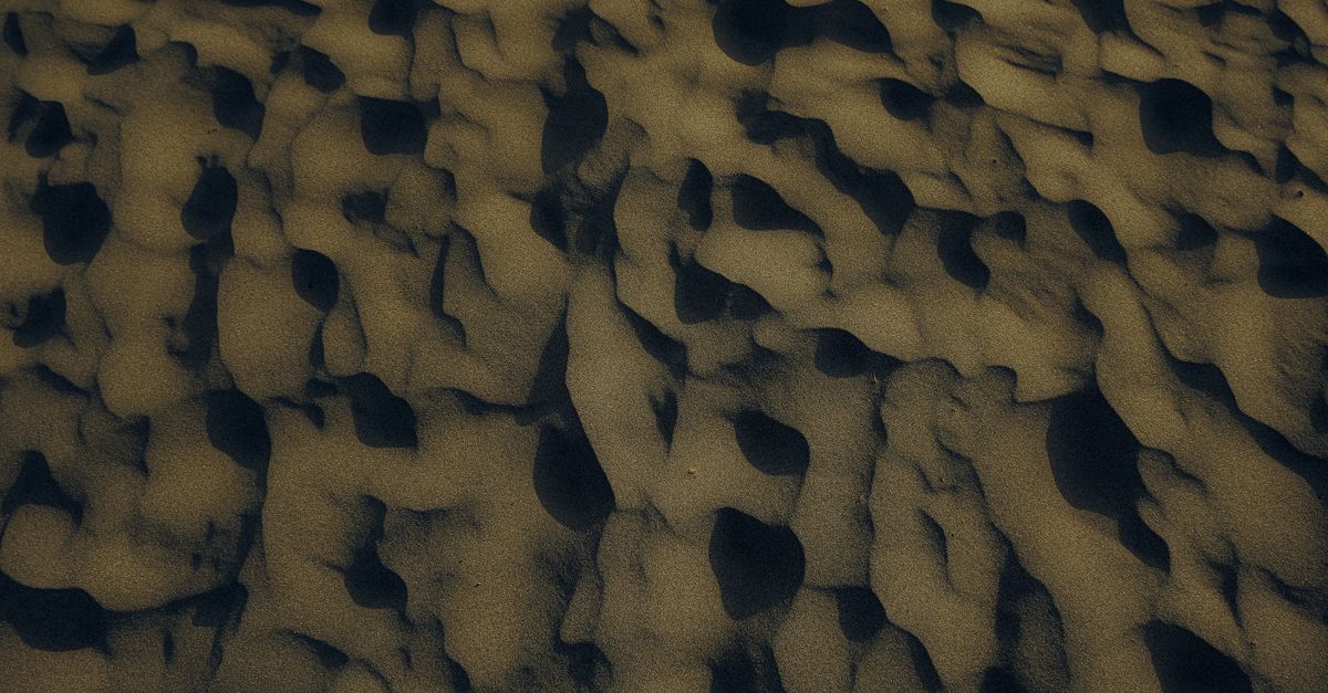 Aerial view of intricate sand patterns on a beach at sunset, capturing nature's artwork.